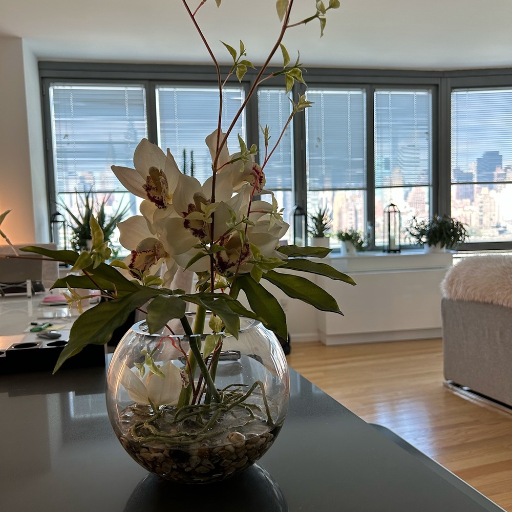 Faux white orchid arrangement with pebbles in glass vase.